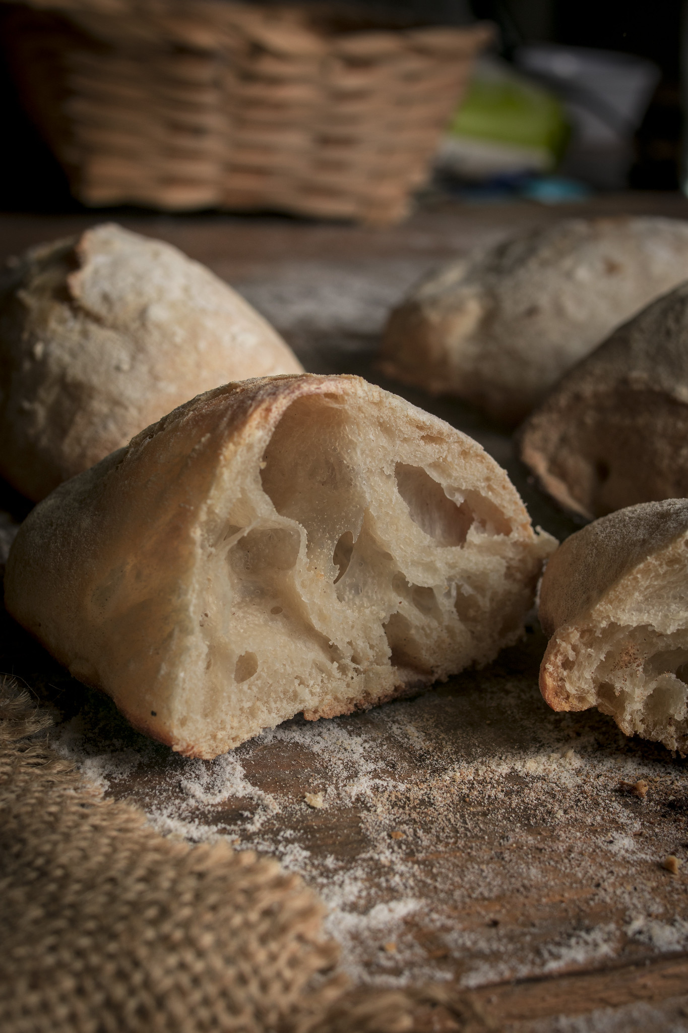 Close-up of torn no-knead ciabatta rolls showing the airy open crumb and flour-dusted crust on a rustic wooden surface.